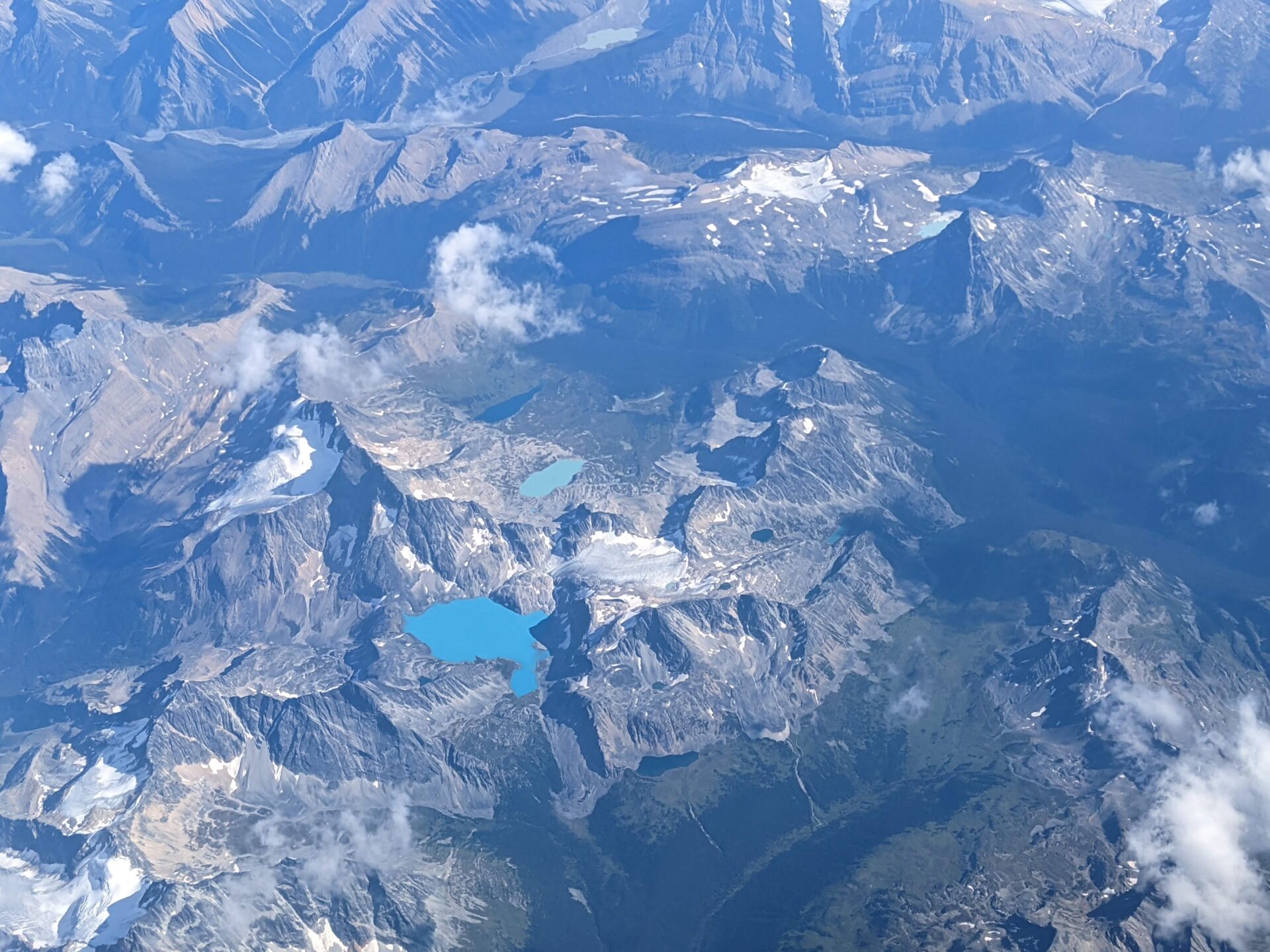 Aerial view of a small, bright blue lake in the middle of a dull-looking mountain range