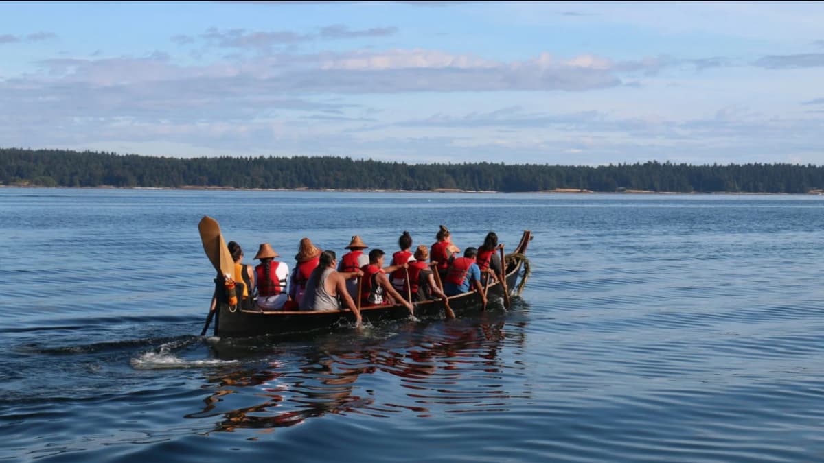 Group of natives in a canoe, all with life vests on, all paddling through the water