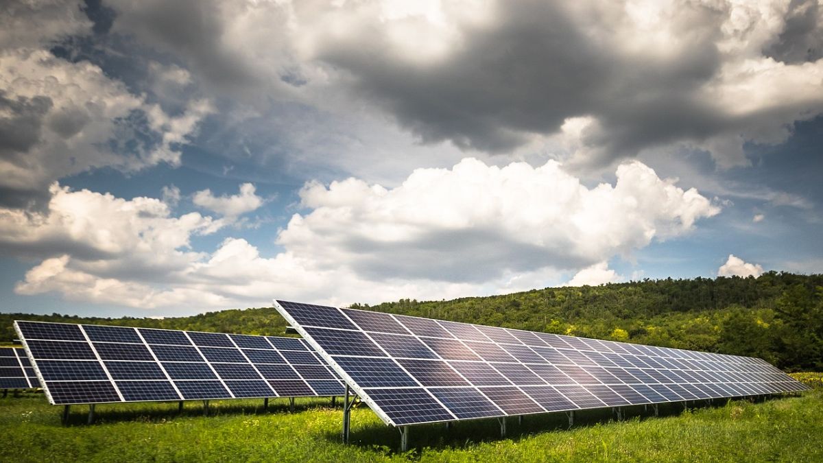 Solar panels on bright green grass and a blue sky full of white clouds in the background