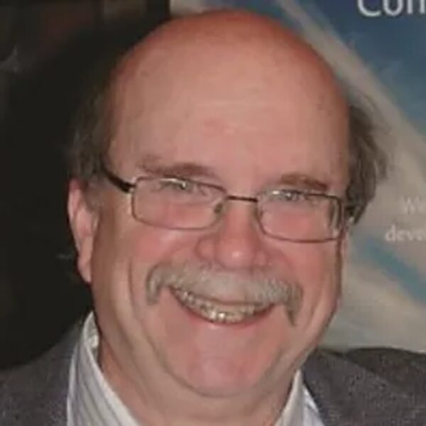 Image of David Johns - brown hair, bald on the top of his head, glasses, a grey mustache, and a big smile