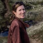 Libbey with a red leather jacket on, sunglasses on her head, with a hiking path background.