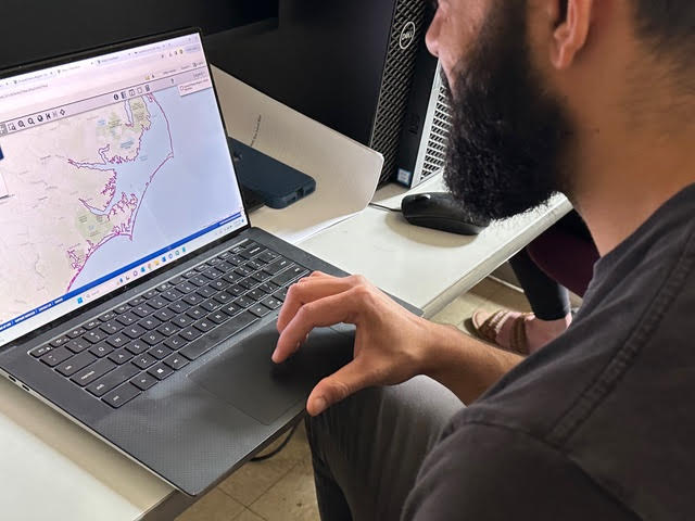 Male student sitting in the classroom using Data Basin on his laptop