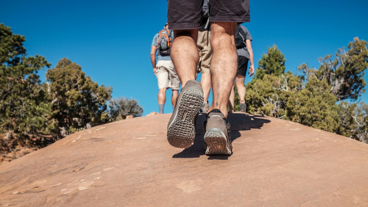 A group of people hiking up a rock on a sunny day. Only their legs and feet are visible.